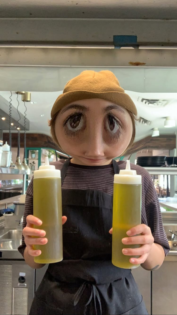Maria Beck, chef and pastry cook, holding two squeeze bottles of herb oil in the kitchen