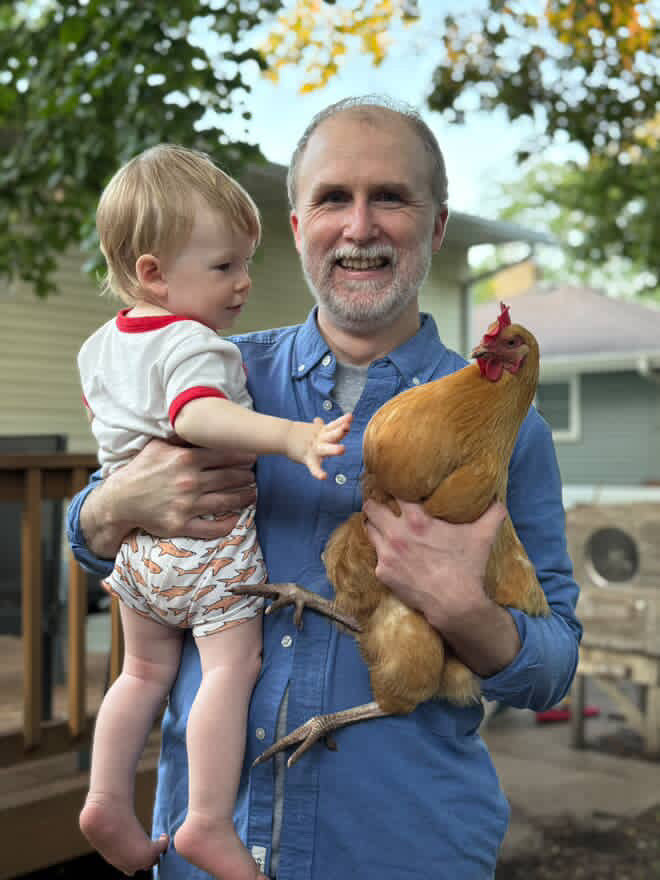 Weston Smith, co-founder and chef, outdoors holding a child and a hen