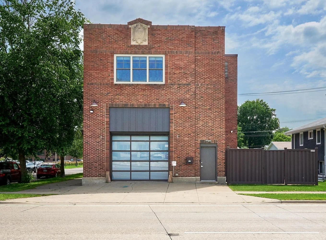 The FIREHOUSE from the street: red brick, the original apparatus bay glazed over, a carved stone cartouche above the upper window.